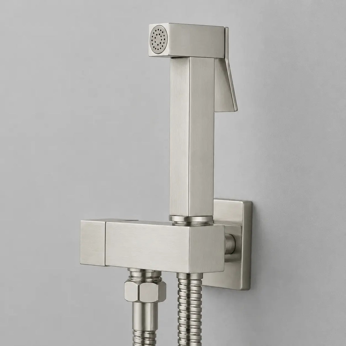 Douchette hygiénique pour WC en acier inoxydable gris brossé, design carré moderne avec flexible et commande intégrée.