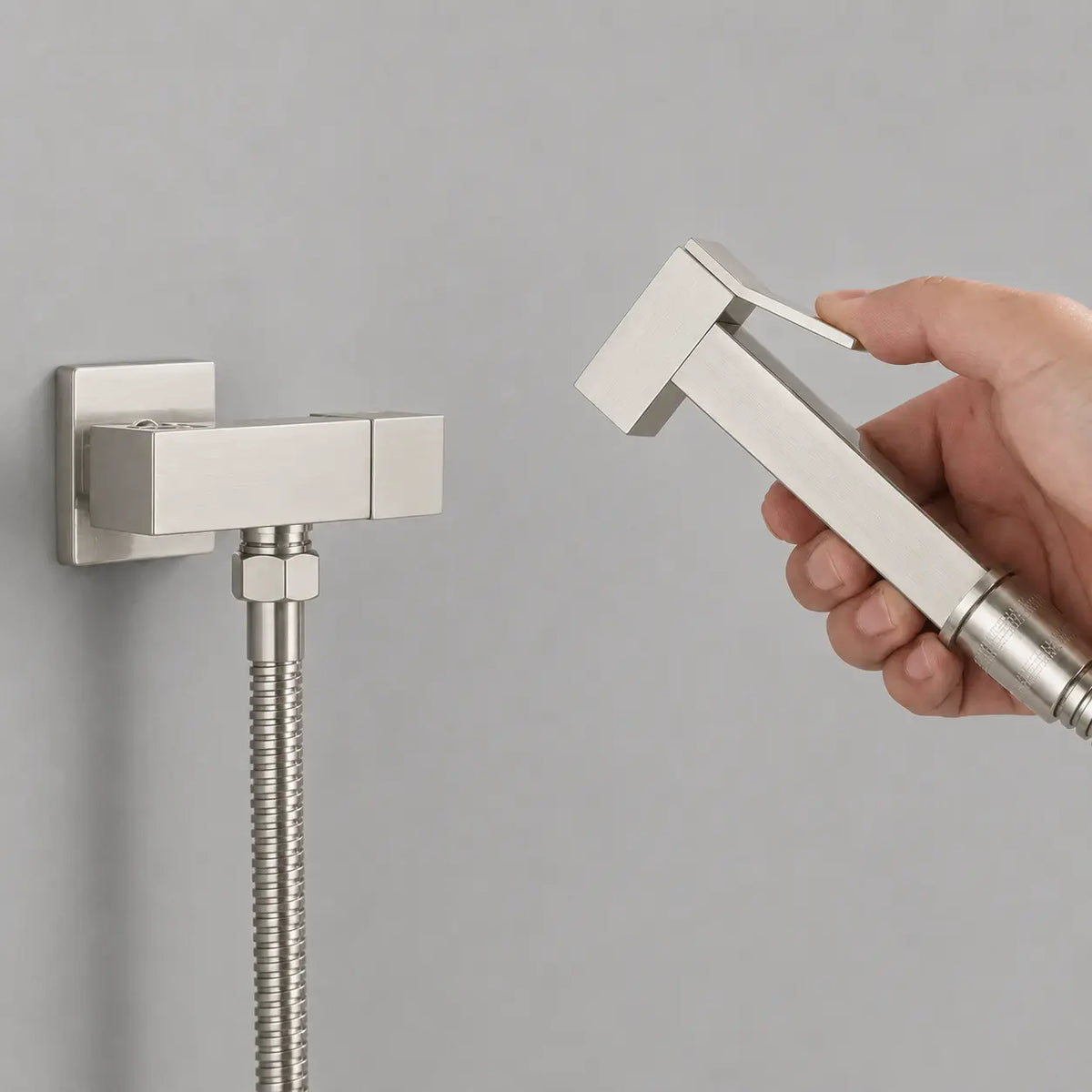 Douchette WC gris brossé tenue en main avec gâchette ergonomique, flexible inox et support mural au design moderne.