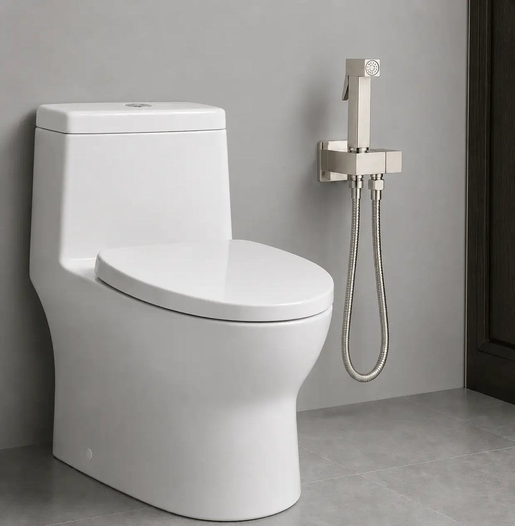 Douchette WC sanitaire gris brossé installée à côté d’un toilette, avec support mural intégré et flexible inox.
