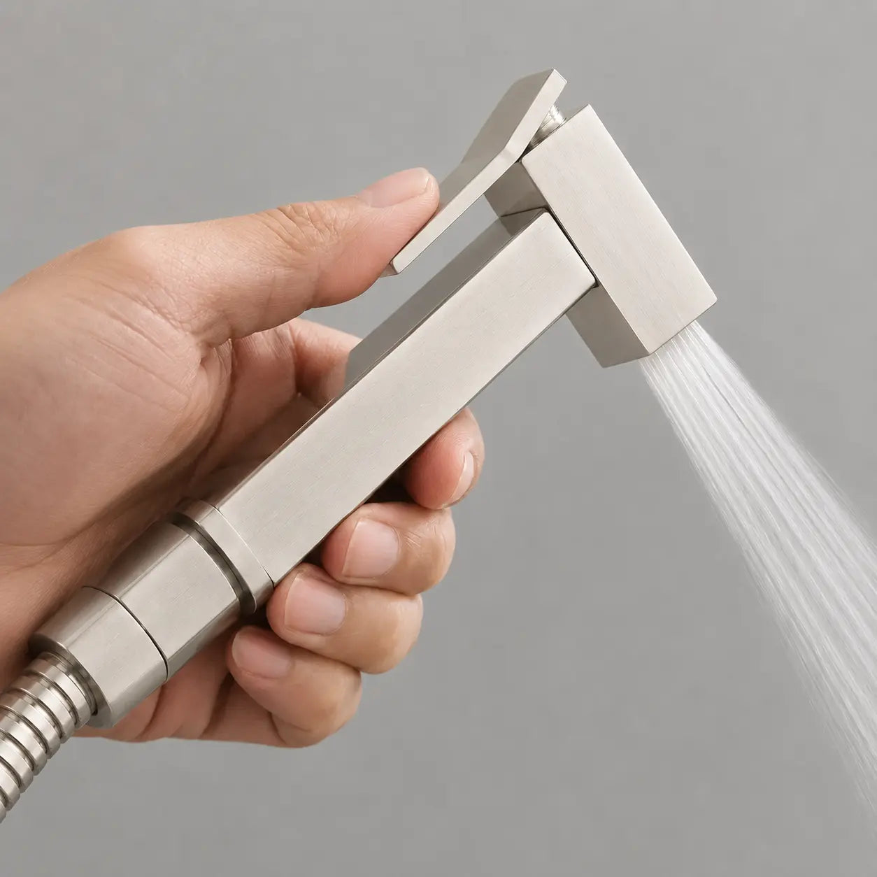 Douchette WC gris brossé en fonctionnement avec jet d’eau précis, gâchette ergonomique et conception carrée moderne. Image
