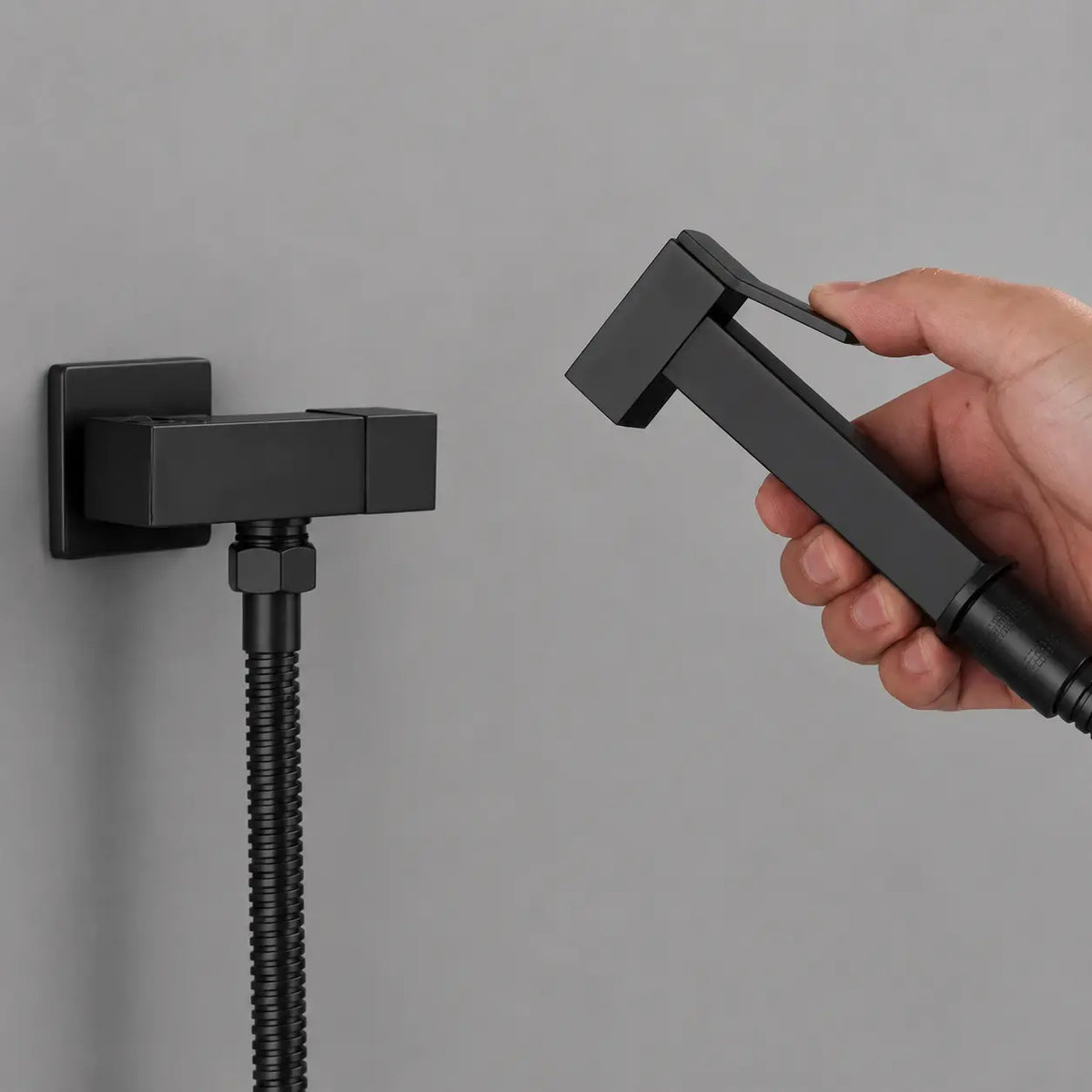 Main tenant une douchette WC noir mat avec gâchette intégrée, design carré moderne et finition élégante.
