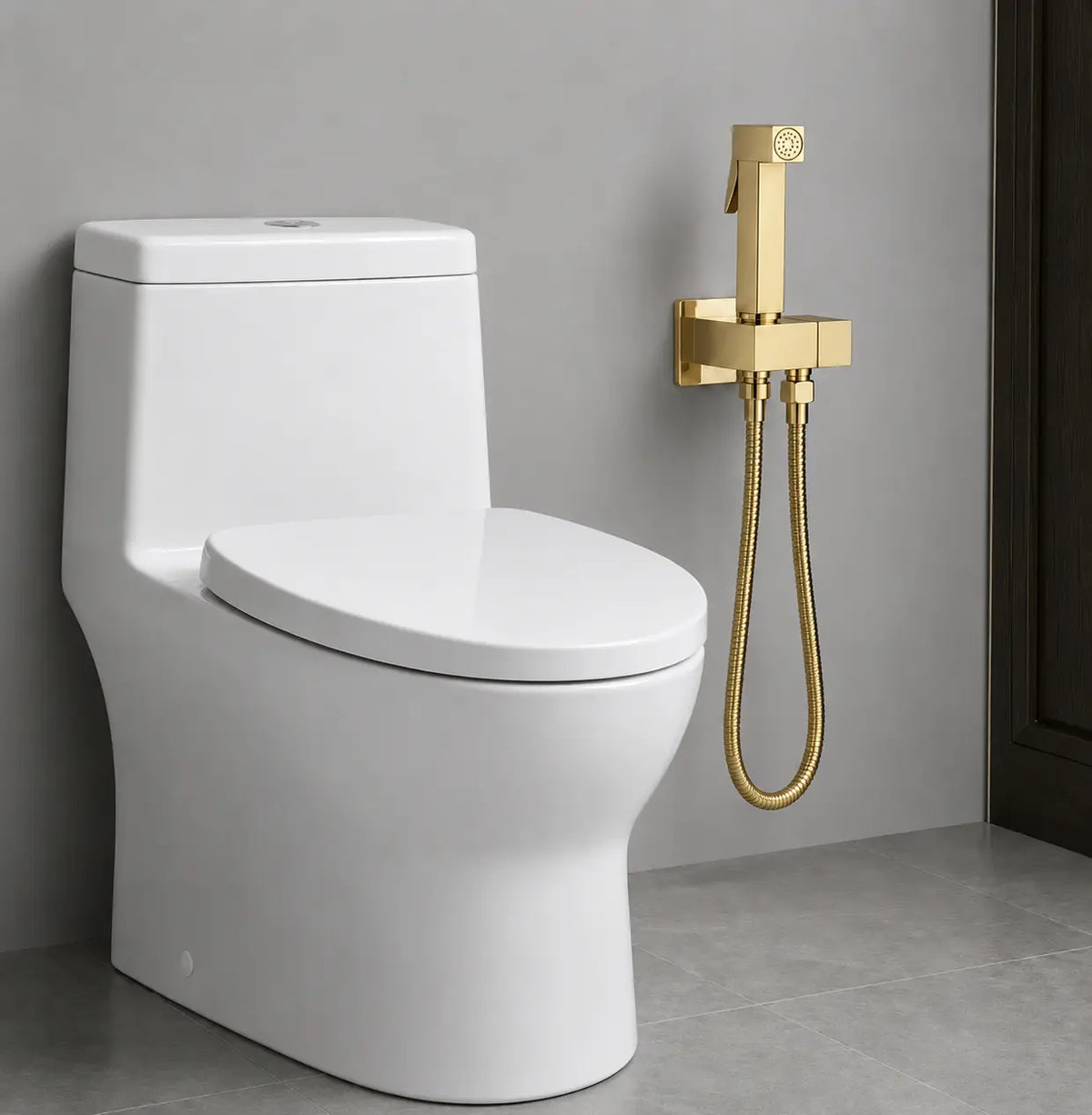 Douchette WC or brossé installée près d’un toilette moderne, avec support mural et flexible métallique assorti.