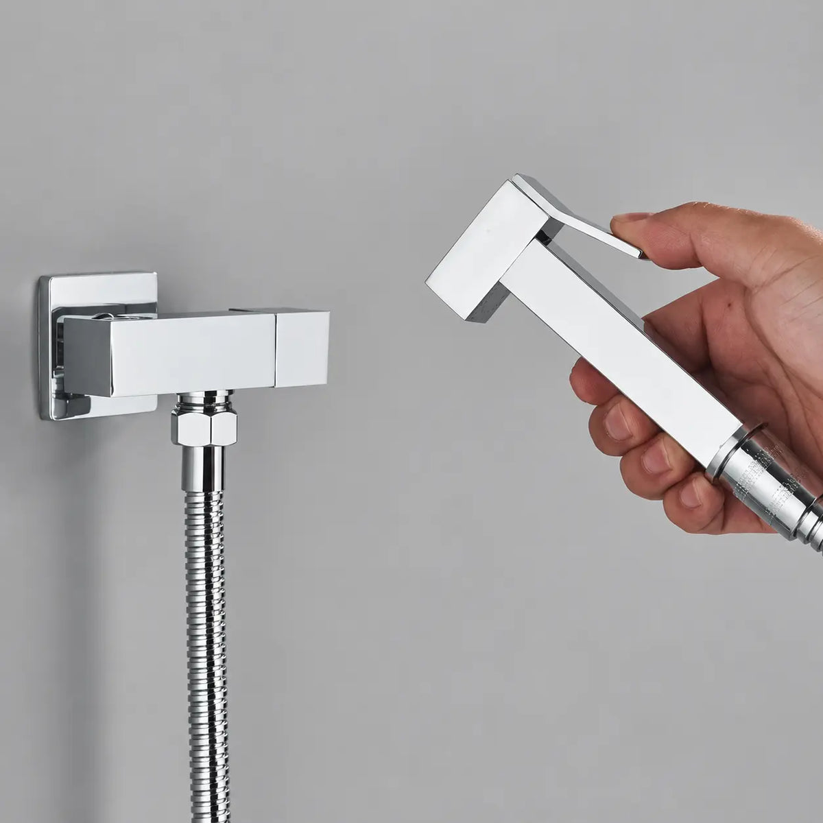 Douchette WC chromée avec poignée ergonomique, flexible inox et support mural au design carré moderne.