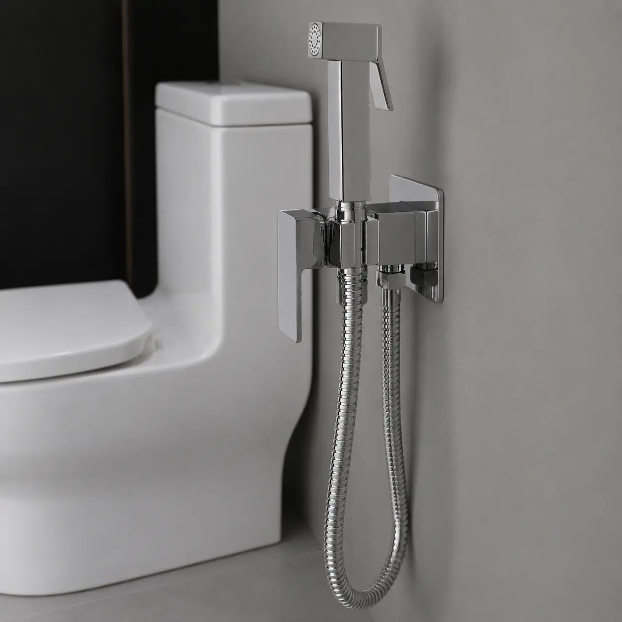 Douchette WC hygiénique chromée avec flexible inox, support mural carré et commande intégrée près des toilettes. Image