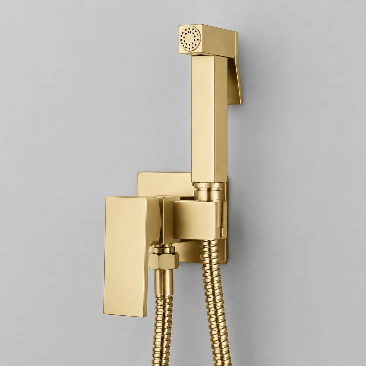 Douchette hygiénique pour WC en or brossé, design carré moderne avec flexible métallique et support mural élégant.