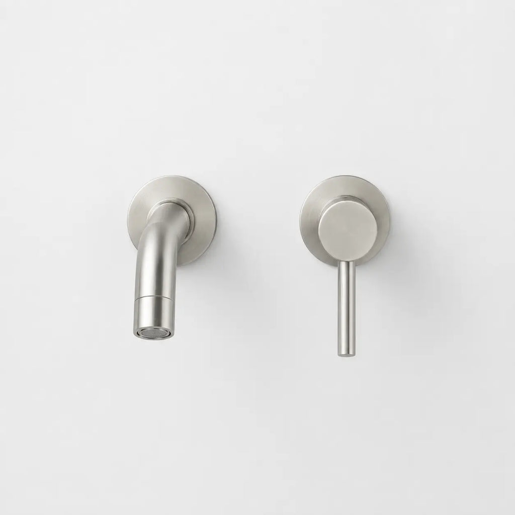 Robinet mural compact en finition gris brossé avec bec court incurvé et commande minimaliste encastrée