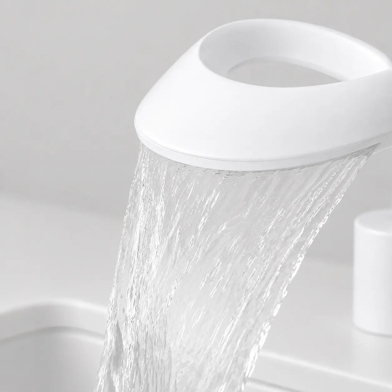 Gros plan du robinet de lavabo cascade blanc en laiton en fonctionnement, avec jet large effet cascade et finition moderne. Image